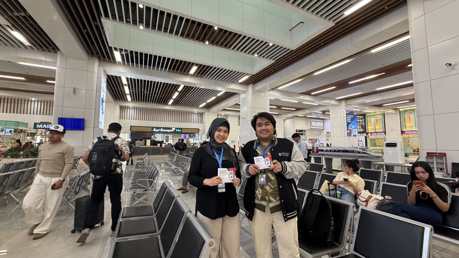 Two members of the survey team holding survey flyers inside Halim HSR Station, Jakarta